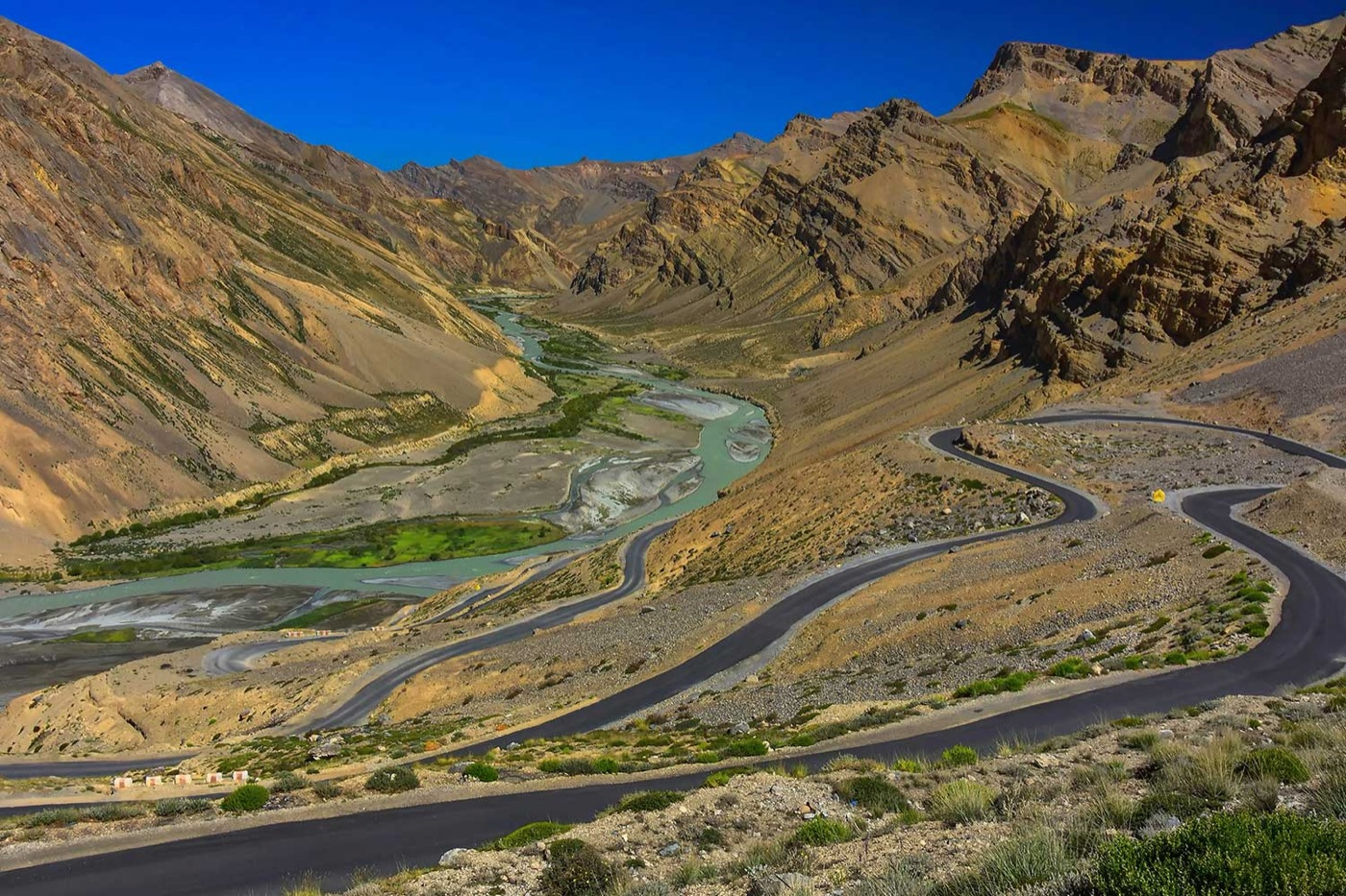 A road switchbacking down a high Ladakh mountain pass into a river valley