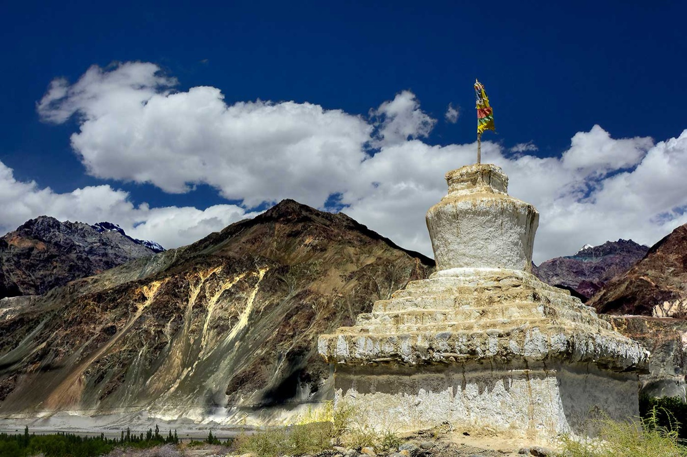 A whitewashed Buddhist chorten with prayer flags against bare Ladakh peaks